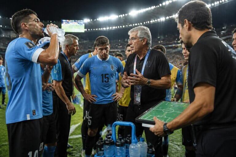 Imagem de jogadores e técnico reunidos na beira do campo durante a parada para hidratação em uma partida de futebol do Mundial 2026 ilustra o post cujo título diz que as pausas para hidratação expõem quem realmente manda na Copa.