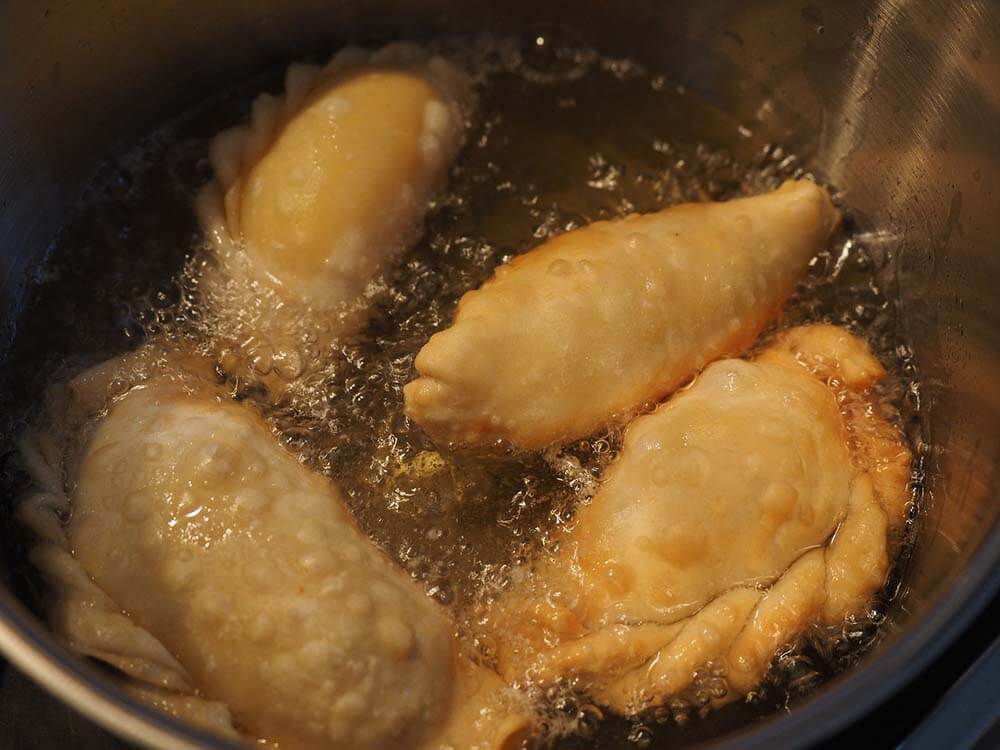 Foto de empanadas sendo fritas numa panela cheia de óleo de cozinha.