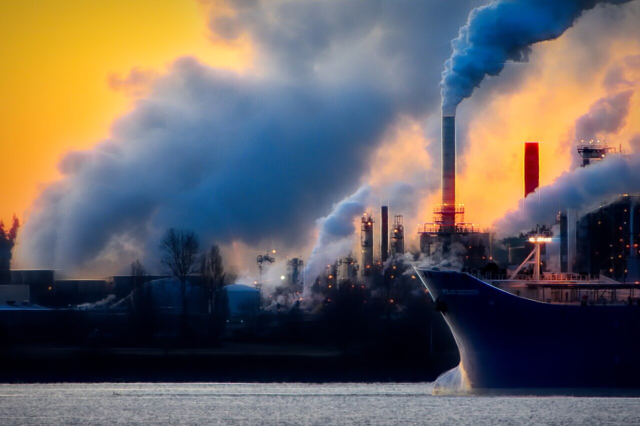 Fumaça sendo expelida por várias chaminés de uma fábrica, sugerindo emissões de gases de efeito estufa