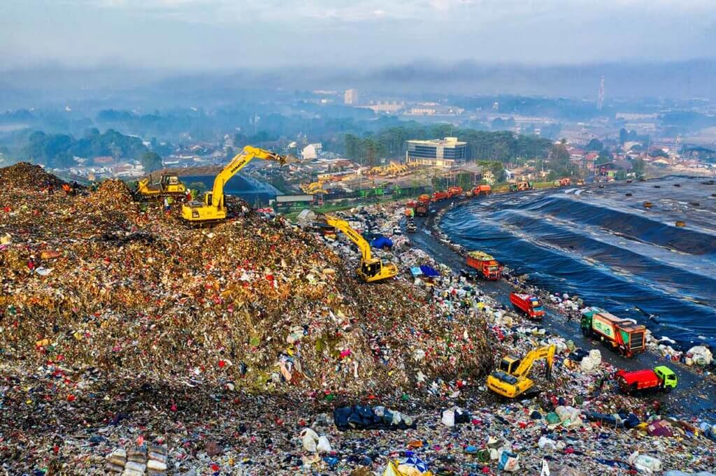 Foto aérea de um aterro sanitário (no pano de frente) e casas residenciais e prédios comerciais (no pano de fundo).