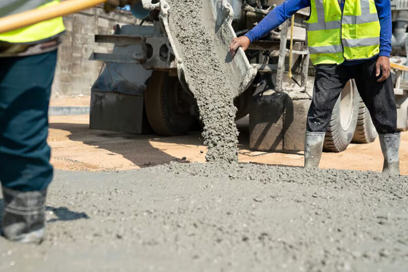 Imagem de dois operários observando uma máquina fazer a concretagem de um piso para ilustrar que um novo tipo de concreto absorve mais CO2 do que emite.