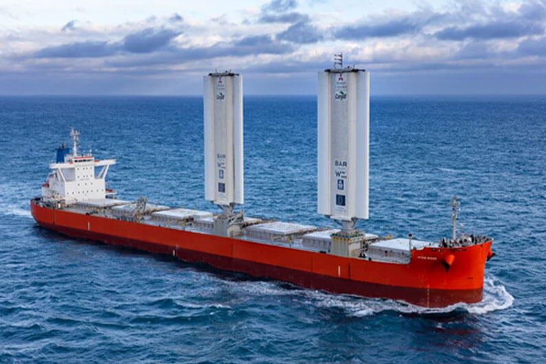 Imagem de um navio cargueiro em um mar azul e navegando com duas torres para captura de vento ilustra o post cujo título diz que navio com asas economiza três toneladas de combustível por dia.