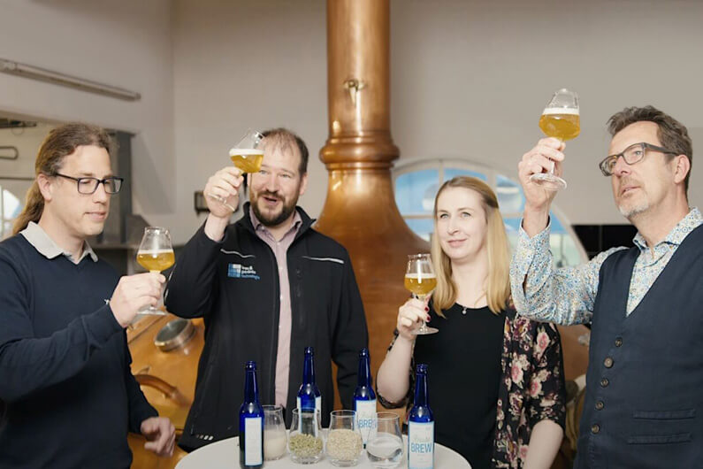 Imagem de três homens e uma mulher, cada um segurando na altura da cabeça uma taça de cerveja pela metade para ilustrar o post que fala de uma cerveja surpreendentemente boa feita com águas residuais.