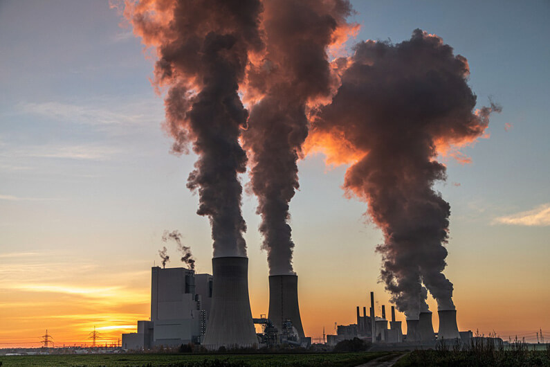 Imagem de uma usina soltando fumaça por quatro chaminés sobe um céu azul claro e pôr do sol ao fundo ilustra o post cujo título é: Remover carbono do ar pode ajudar a conter o aquecimento global