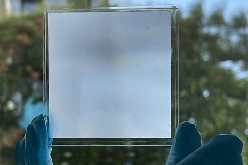 Imagem de uma placa de metamaterial multifuncional microfotônico sendo segurada por duas mãos com luvas azuis ilustra o post cujo título diz que um novo material mais transparente do que o vidro é autolimpante.
