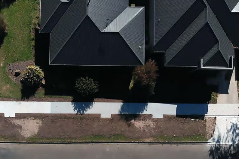 Imagem aérea mostrando o telhado de duas casas ao lado da calçada para pedestres e parte do asfalto da rua ilustra o post cujo título diz que um super concreto reforçado com café vai começar a ser testado.
