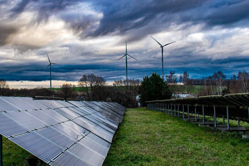 Imagem de painéis solares e torres eólicas numa área bem verde ilustra o post cujo título aborda: O que são 'pontos positivos de inflexão' climática?