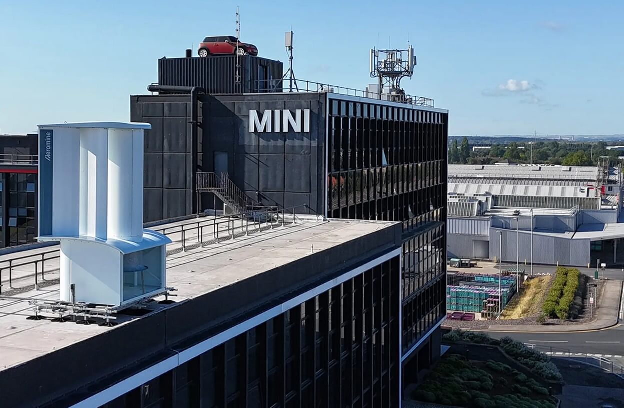 Imagem de uma turbina eólica imóvel instalada no topo do prédio da fabricante do veículo MINI, da BMW, ilustra o post cujo título diz que as turbinas eólicas imóveis geram energia de forma bem eficiente.