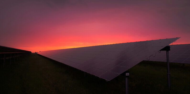 Imagem de placas solares sobre um campo gramado debaixo de um céu alaranjado pelo pôr do sol ilustra o post cujo título diz que os empregos verdes tiveram o maior crescimento de todos os tempos.