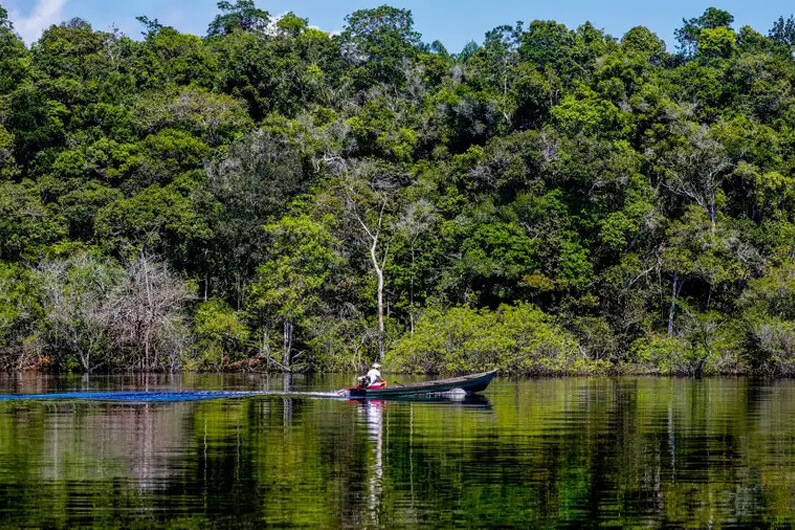 Imagem de uma pessoa navegando com uma canoa pelo Rio Negro com a Floresta Amazônica ao fundo ilustra o post cujo título diz que o Brasil anda em corda bamba diplomática e ambiental de alto risco.