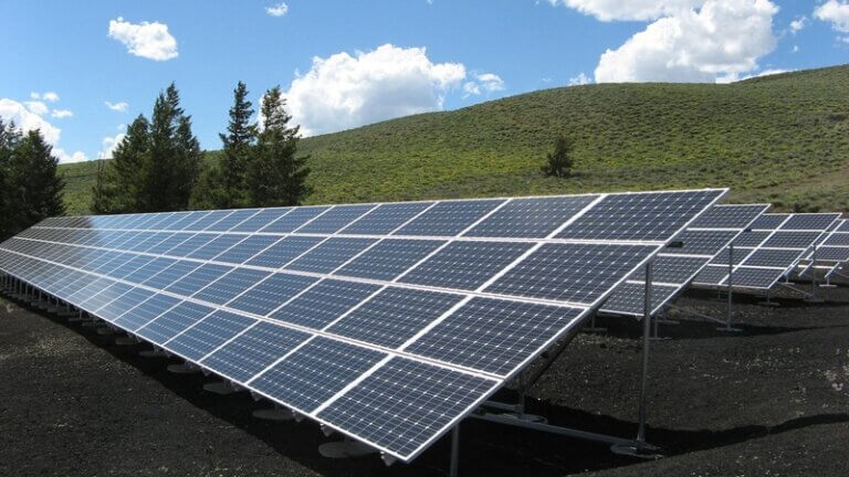 Imagem de várias placas solares instaladas em um terreno gramado, arborizado e sob um céu azul ilustra o post cujo título diz que o investimento global em energia limpa bate recorde em 2025.