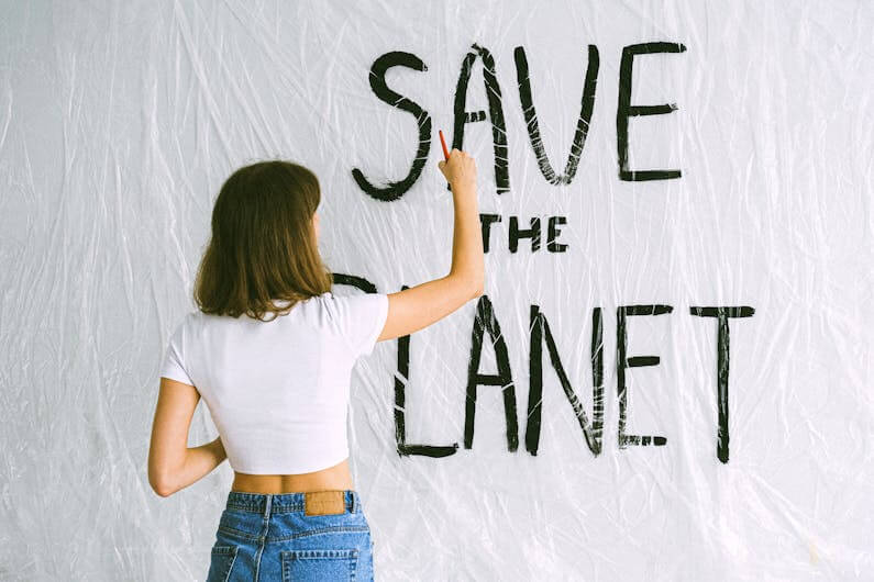 Imagem de uma mulher escrevendo na parede a expressão "SAVE THE PLANET" ilustra o post cujo título diz que a JBS e outras gigantes do ramo fazem promessas net zero vazias.