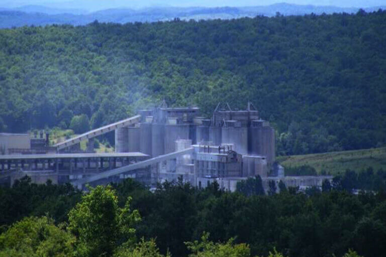 Imagem de uma fábrica de cimento no meio de uma área totalmente verde ilustra o post que diz que a eletricidade pode produzir cimento com pegada mínima de carbono.