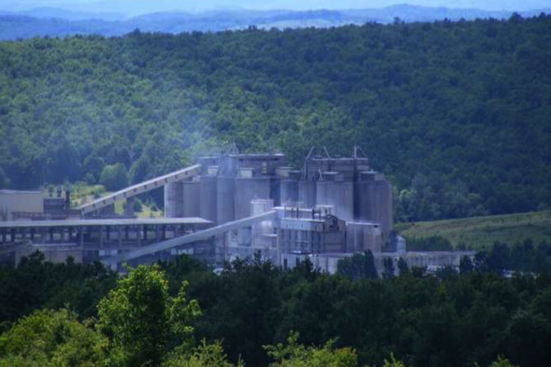Imagem de uma fábrica de cimento no meio de uma área totalmente verde ilustra o post que diz que a eletricidade pode produzir cimento com pegada mínima de carbono.