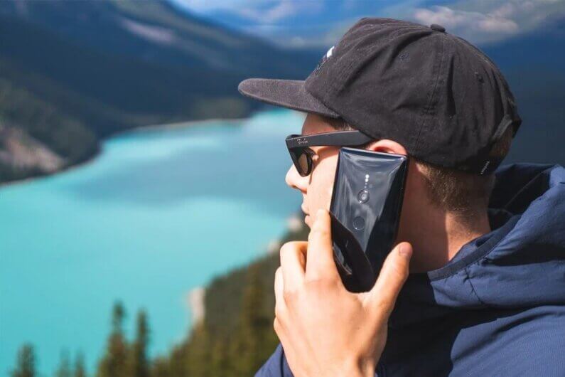 Imagem de um rapaz que usa boné e óculos escuros e fala ao celular ao ar livre ilustra o post cujo título diz que a Amazon está fazendo uma rede de telefonia com 5 mil satélites.