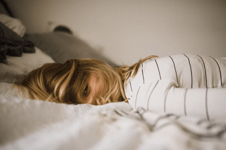 Imagem de uma mulher deitada na cama e aparentemente exausta ilustra o post cujo título pergunta: Por que seu corpo está destruído, mas a mente não quer dormir?