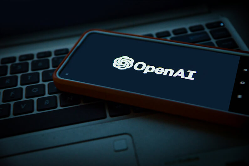Imagem do nome OpenAI que aparece na tela de um celular que está sobre o teclado de um laptop ilustra o post cujo título diz que a OpenAI reduz desenvolvimento de IA avançada após ciberataque.