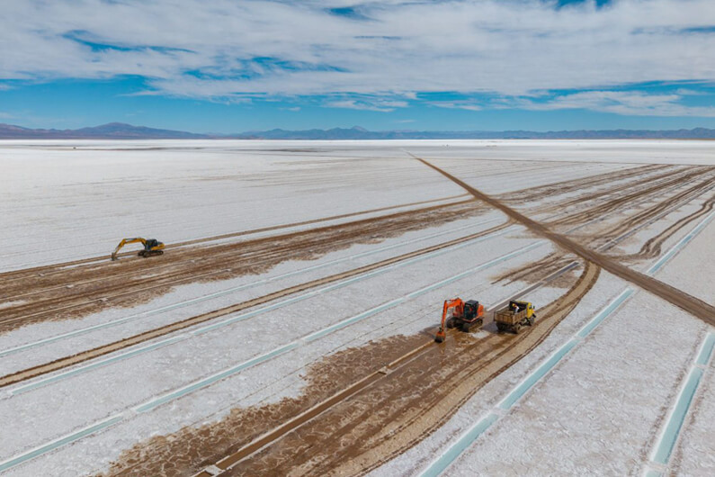 Imagem do deserto de sal de Salinas Grande com máquinas trabalhando na extração sob um céu metade azul e metade com nuvens ilustra o post cujo título diz que a A Argentina precisa tomar as rédeas de seus minerais críticos.