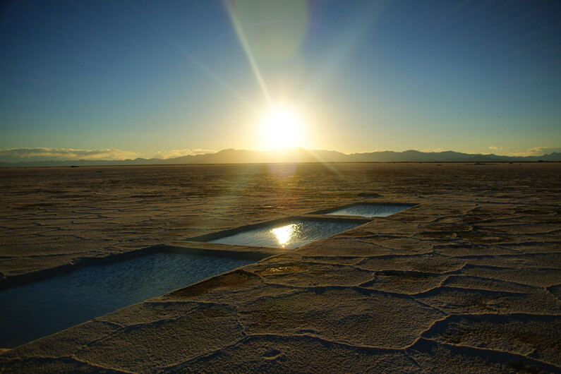 Imagem de piscinas de evaporação sob um céu azul e o pôr do sol no horizonte da região de Salinas Grande ilustra o post cujo título diz que a A Argentina precisa tomar as rédeas de seus minerais críticos.
