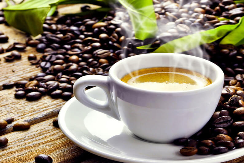 Imagem de uma xícara branca cheia de cappuccino e fumaça saindo da mesma ilustra o post cujo título diz que a temperatura do seu chá ou café está ligada ao câncer.