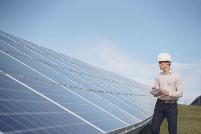 Imagem de um trabalhador usando um capacete branco e ao lado de placas solares ilustra o post cujo título diz que os empreendimentos verdes em estágio inicial podem gerar bons empregos.