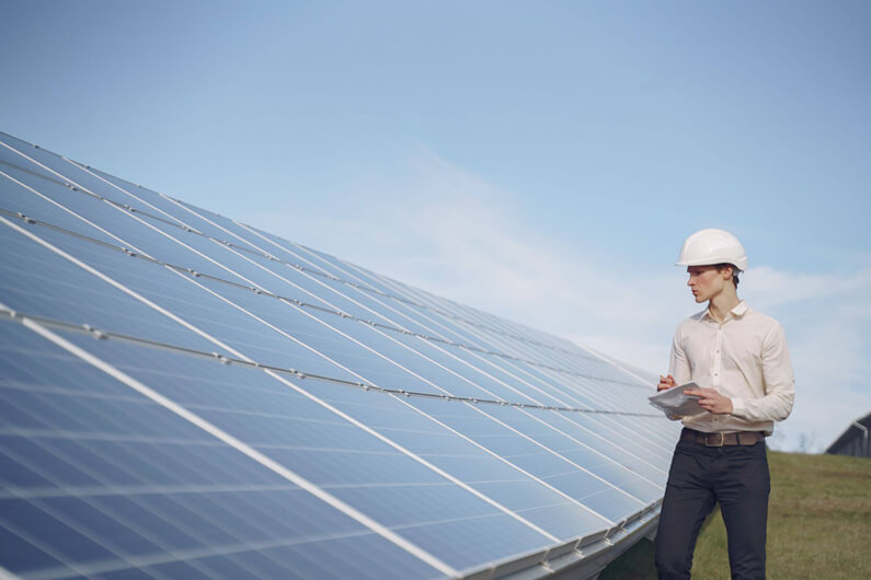 Imagem de um trabalhador usando um capacete branco e ao lado de placas solares ilustra o post cujo título diz que os empreendimentos verdes em estágio inicial podem gerar bons empregos.