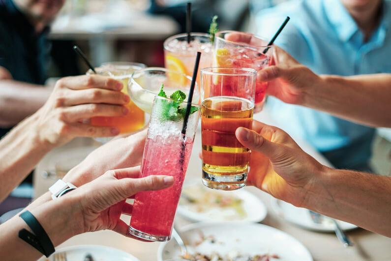 Imagem de cinco mãos aparentemente masculinas seguram cinco copos com drinks ao fazerem um brinde ilustra o post com o título: Meningite nas universidades: por que o risco é maior entre alunos.