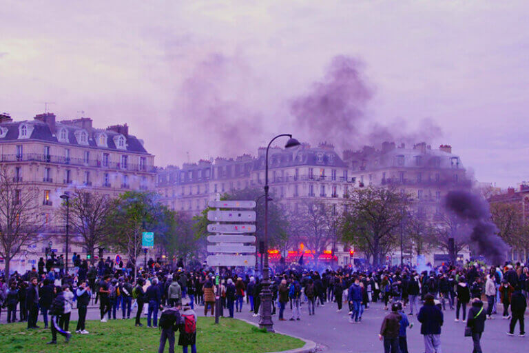 Imagem de uns prédios em meio a muita fumaça e muitas pessoas protestando em uma praça de Paris ilustra o post sobre como a crise climática impulsionou os protestos na França.