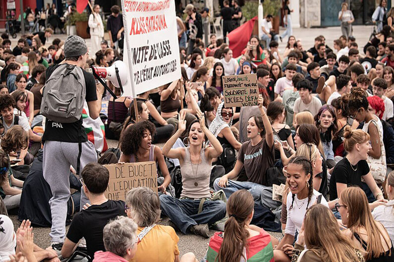 Imagem de alunos do ension médio sentados no chão de uma rua da França e ostentando cartazes ilustra o post sobre como a crise climática impulsionou os protestos na França.