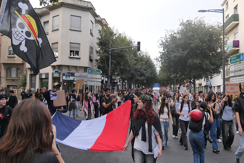 Imagem de alunos do ension médio caminhando pelas ruas da França e ostentando cartazes e a bandeira francesa ilustra o post sobre como a crise climática impulsionou os protestos na França.