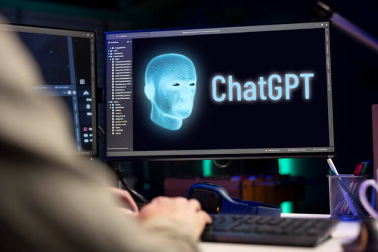 Imagem de um braço repousando sobre um teclado de computador abaixo de um monitor que mostra uma face robótica e o nome ChatGPT ilustra o post com o título: A OpenAI diz que seus agentes de IA desativaram suas próprias travas de segurança.