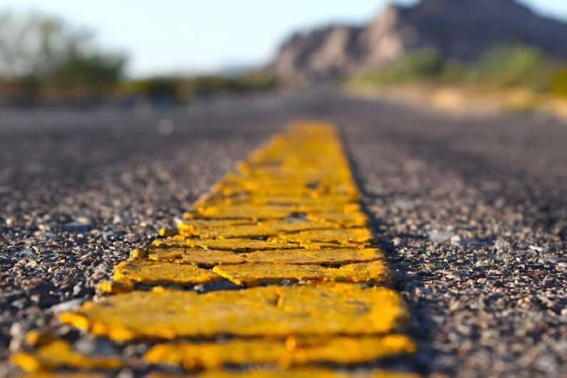 Imagem de uma estrada mostrando o asfalto com uma faixa amarela pigmentada ilustra o post cujo título diz que o asfalto com plástico reciclado melhora o pavimento e reduz as partículas plásticas.